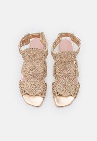 Guld sandaler med intrikata blommönster i spetsdesign och fyrkantig tå. Guld metalliska detaljer på sulan och en vadderad innersula. Öppen bak.