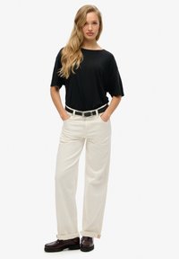 Camiseta negra de gran tamaño con mangas cortas, combinada con pantalones de pierna ancha en color crema, un cinturón negro y mocasines oscuros con suela texturada.