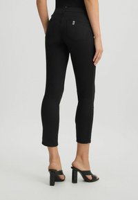 Jeans negre, ajustate, cu talie medie, având detalii de cusătură subtile și două buzunare spate. Îmbrăcate cu sandale negre cu toc bloc.