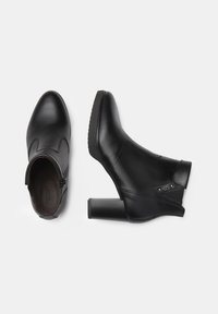Bottines en cuir noir avec un design courbé, fermeture éclair sur le côté, talon carré texturé et accents subtils près de la cheville.