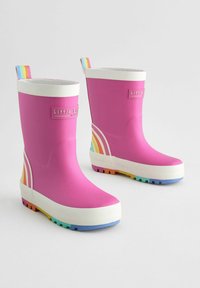 Bottes de pluie en caoutchouc rose avec un bandeau supérieur blanc, un accent rayé arc-en-ciel sur le côté et des semelles multicolores. Elles disposent d'une poignée de traction.
