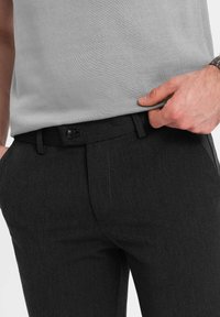 Zwarte pantalon met een gladde textuur, voorzien van een enkele knoopsluiting en zijzakken. Gepaard met een lichtgrijze top.