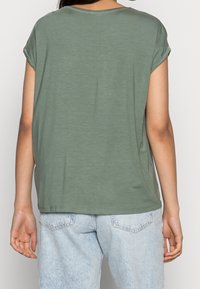 Grön kortärmad t-shirt med avslappnad passform, gjord av mjukt material, med rund halsringning och rullade ärmar, ihop med ljusa denimjeans.