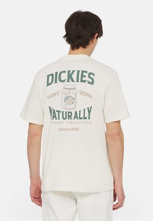 Mand iført cremehvid T-shirt med "Dickies Naturally Home Grown Finest Products Since 1922" og bøtte grafik på ryggen.