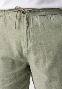 Lichgroene linnen broek met een elastische tailleband, een trekkoordsluiting en twee zijzakken. Heeft een discrete textuur en gouden hardwareaccenten.