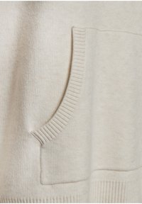 Svetre v svetlo bež barvi, ki se ponaša z teksturiranim pletenjem, vidno sprednjo žepno z ribanim robom in ribanim robom na dnu. Gladek material z nežnim videzom.
