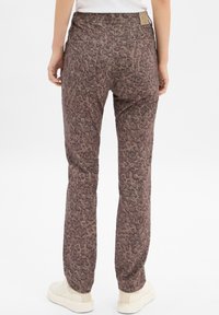 Pantalons à imprimé léopard dans une combinaison de couleurs marron et beige ; présentent une coupe décontractée, une taille élastique et deux poches arrière. Portés avec des baskets crème.