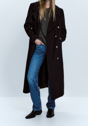 Zwarte dubbelgeknoopte jas van een wolmix, met grote knopen, een reverskraag en een lange silhouet, gedragen over een grijze trui en blauwe spijkerbroek.
