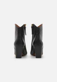 Bottes de cheville en cuir noir avec des talons carrés et des détails de fermeture éclair dorée, présentant une texture lisse et un design épuré et pointu.