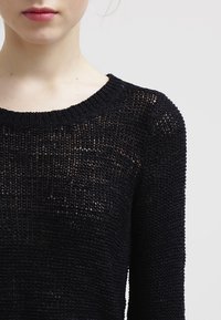 Schwarzer Strickpullover mit weitem Ausschnitt, lockerer, strukturierter Musterung und dreiviertellangen Ärmeln.