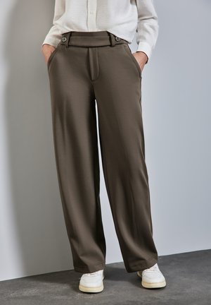 Pantaloni a gamba larga marroni realizzati in tessuto liscio, con vita alta, tasche frontali e dettagli con bottoni, abbinati a sneakers bianche.