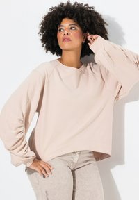Světle béžová oversized mikina s kulatým výstřihem a nabíranými balónovými rukávy, doplněná o světle šedé texturované kalhoty. Jednoduchý design, měkká tkanina.