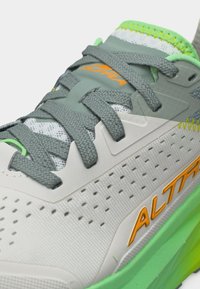 Κοντινό πλάνο γκρι και λευκού αθλητικού παπουτσιού με πράσινες και πορτοκαλί λεπτομέρειες, γκρι κορδόνια, διάτρητο πλαϊνό πάνελ και σήμανση "Altra".