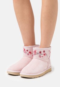 Botas de tobillo de ante rosa con bordados florales en tonos rojos y rosas, con un interior suave y suela de goma.
