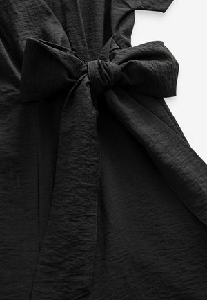 Mustal dress, mis on valmistatud tekstuursest kangast, lühikeste varrukatega ja silmapaistva sõlme detailiga vööl, rõhutades selle elegantset siluetti.