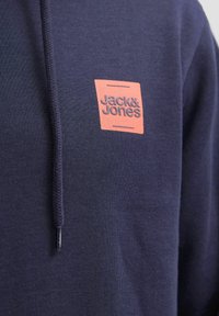 Navy blue hoodie made of soft fabric, featuring a rectangular orange logo with "Jack & Jones" text on the chest and a drawstring hood.