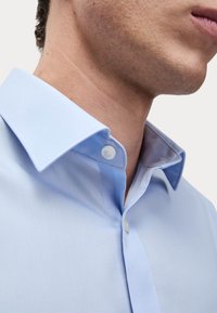 Hellblaues Hemd mit strukturiertem Kragen, Knopfleiste und glattem Stoff. Der Innenkragen kontrastiert mit einem dunkleren Blauton.