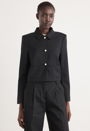 Zwarte cropped jacket met een kraag, gouden knopen en twee voorzakken. Soepele textuur, lange mouwen, gecombineerd met zwarte broeken.