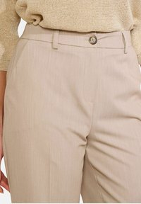 Bēša krāsas piegrieztas bikses ar smalku svītru rakstu, ar pogu aizdari, sānu kabatām un gludu tekstūru.