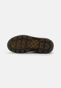 Suola di una scarpa nera con un motivo di battistrada testurizzato, che mostra più scanalature orizzontali e sezioni in gomma rialzate per la presa.