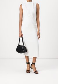Robe midi blanche sans manches avec des détails froncés à la taille ; associée à des sandales à talons noirs et un petit sac à main noir.