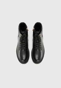 Botas de cuero negras con una textura suave, que cuentan con un cordón tradicional, dos cremalleras doradas y una punta redondeada. Diseño de suela plana.