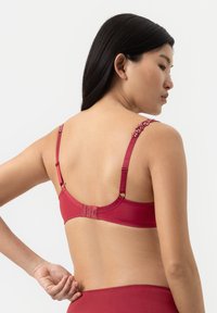 Rode beha van gladde stof, decoratieve bandjes met kleine details en een haak- en oogsluiting aan de achterkant. Verstelbare bandjes voor een goede pasvorm.