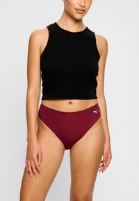 Top noir sans manches avec une texture côtelée, associé à un bas de bikini taille haute bordeaux avec un logo sur le côté.