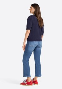 Short-sleeve navy sweater made of soft material, paired with light blue cropped jeans. Red shoes with white laces and textured soles.