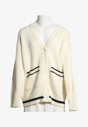 Cardigan en maille crème avec des détails de rayures noires sur les poches et l’ourlet, fermeture à boutons sur le devant, et col en V sur un mannequin blanc.