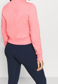 Sudadera rosa corta con borde acanalado y cuello alto, combinada con leggins marinos. Textura suave, manga larga y forma ajustada.