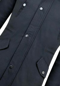 Zwarte stoffen jas met een knoopsluiting aan de voorkant, twee zijzakken met klep en een gladde textuur. Geaccentueerd met zilverkleurige knopen voor sluiting.