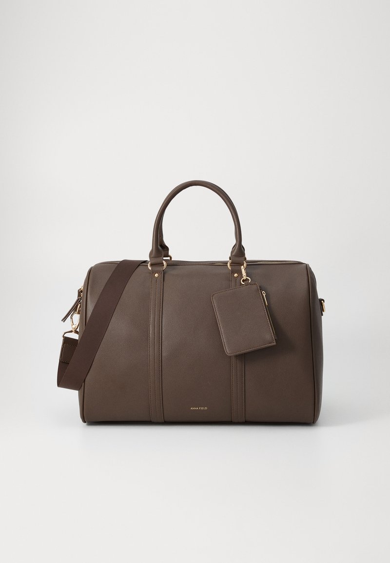Brown leather duffel bag with gold hardware, dual handles, and a detachable shoulder strap. Includes a matching luggage tag. Textured finish.