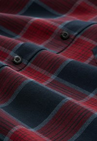 Karierter Hemd in Rot- und Marineblau mit kontrastierenden grauen Linien. Der Stoff ist weich und die Knöpfe sind sichtbar.