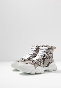 Wysokie sneakersy z czarnym i szarym wzorem w węża, białymi sznurówkami i masywną białą podeszwą, z teksturowanym materiałem i detalami akcentującymi.