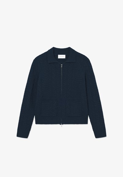 Navy blue knitted cardigan with a zippered front, ribbed collar, and two patch pockets featuring textured cable-knit patterns.
