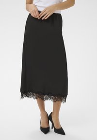 Jupe midi noire en satin avec une taille  élastique et une bordure en dentelle délicate à l'ourlet. Associée à des chaussures à talons hauts noires.