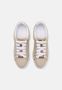 Beiga syntetiska sneakers med vita snören, präglad logotyp och guld accenter. Slät textur med rund tå och vadderad innersula.