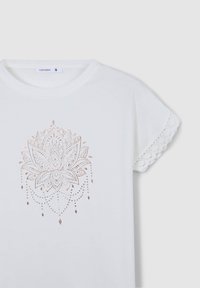 Biała koszulka z różowo-złotym wzorem kwiatu lotosu na środku, z koronkowymi akcentami na rękawach dla dodatkowej tekstury. Rozmiar mały.