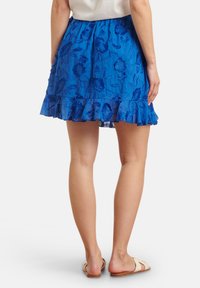 Blauwe, geborduurde rok met bloemenpatronen, een rimpelrand en een aansluitende tailleband. Geloosd met platte, open teen sandalen.