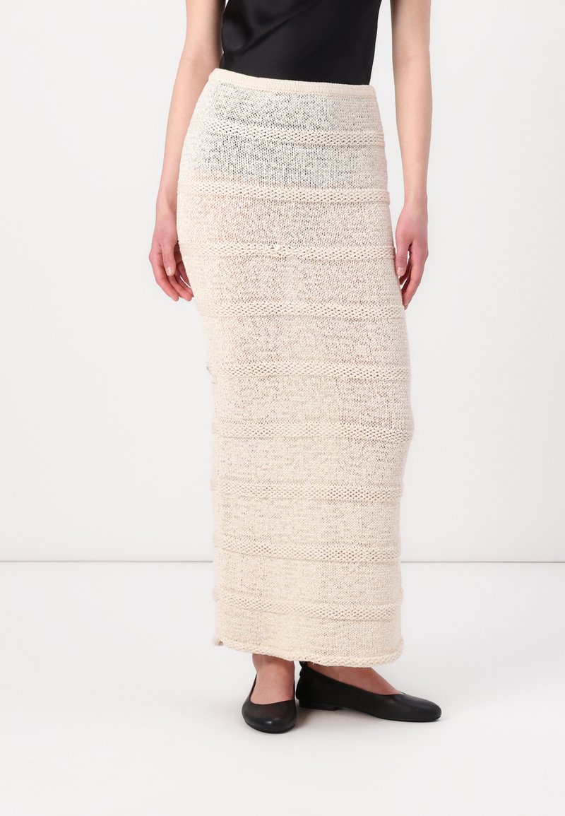 Jupe maxi en tricot de couleur crème avec des rayures horizontales texturées et une taille ajustée, associée à des chaussures plates noires.