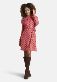 Red long-sleeve dress with a wave pattern, tie waist detail, and A-line shape. Paired with brown knee-high suede boots.