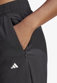 Schwarze Sporthose mit glatter Oberfläche, ausgestattet mit einem elastischen Bund und einer seitlichen Reißverschlusstasche. Adidas-Logo in Weiß an der unteren Beinseite.