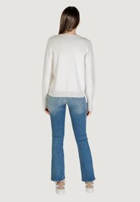 Witte gebreide trui met een relaxed fit, bootnek, ribbelzoom; gecombineerd met blauwe flared jeans en lichtgekleurde sneakers.