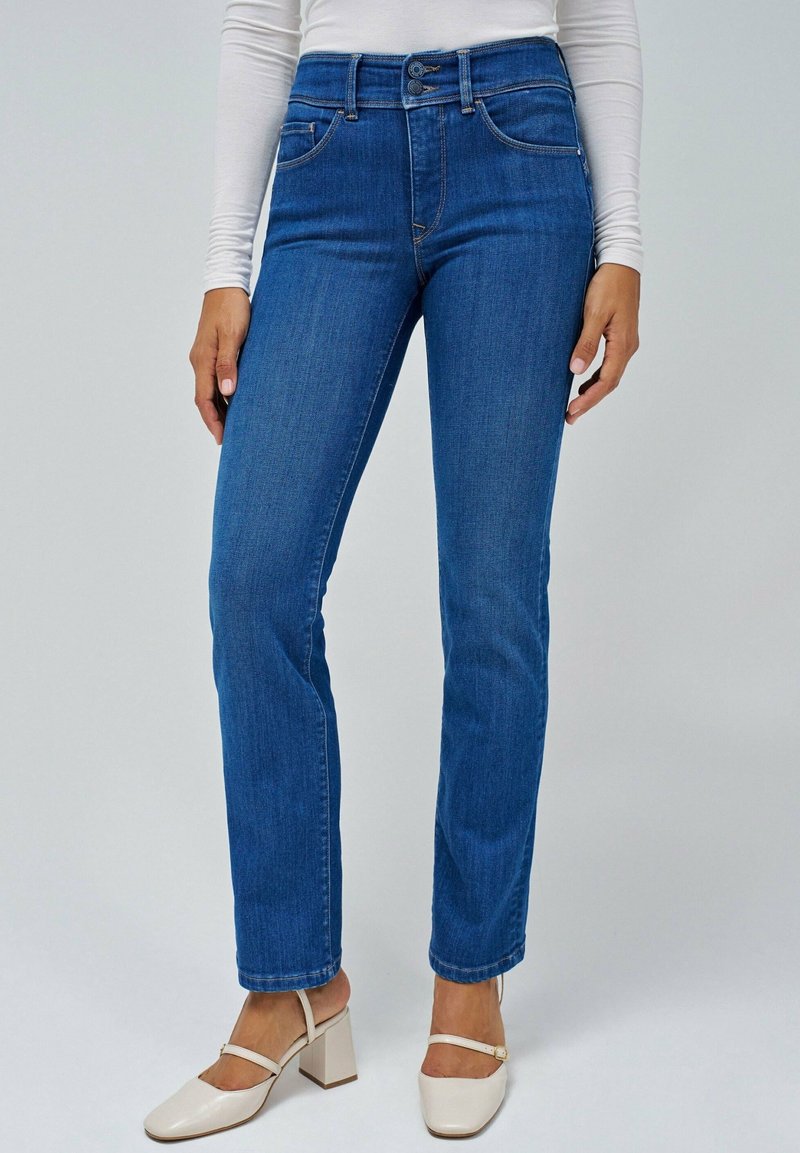 Jeans bleus avec un design à jambe droite, fabriqués en denim. Présentent des poches avant et une fermeture à bouton. Association avec des chaussures à talons carrés crème.