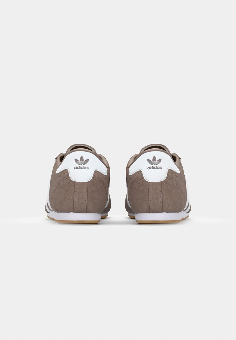 Braune Wildlederschuhe mit weißen Akzenten, ausgestattet mit einem runden Absatz, einem Logo auf dem Absatz und drei weißen Streifen an der Seite.