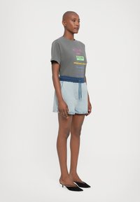 Grå t-skjorte med flerfarget tekst, kombinert med lyseblå denimshorts med mørkeblå snor i livet og svarte hælsandaler.