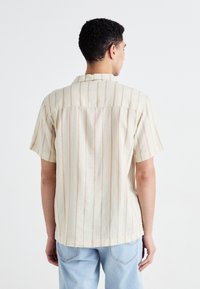 Short-sleeve shirt in light beige fabric with thin orange stripes, featuring a relaxed fit and a collar. Back view showcases shoulder yoke design.
