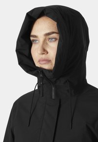 Chaqueta negra con capucha, con cremallera en la parte frontal, cordones ajustables y un acabado suave y mate. Presenta un cuello alto y un diseño sin costuras.