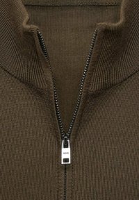 Suéter marrón de punto con cremallera y cuello alto, que presenta una cremallera negra y un tirador plateado, mostrando una textura acanalada.
